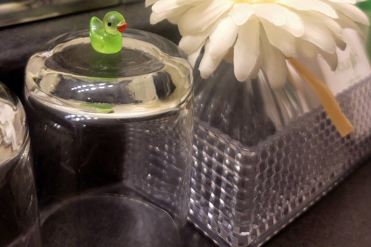 Un récipient en verre contenant une figurine de canard verte et une fleur blanche.