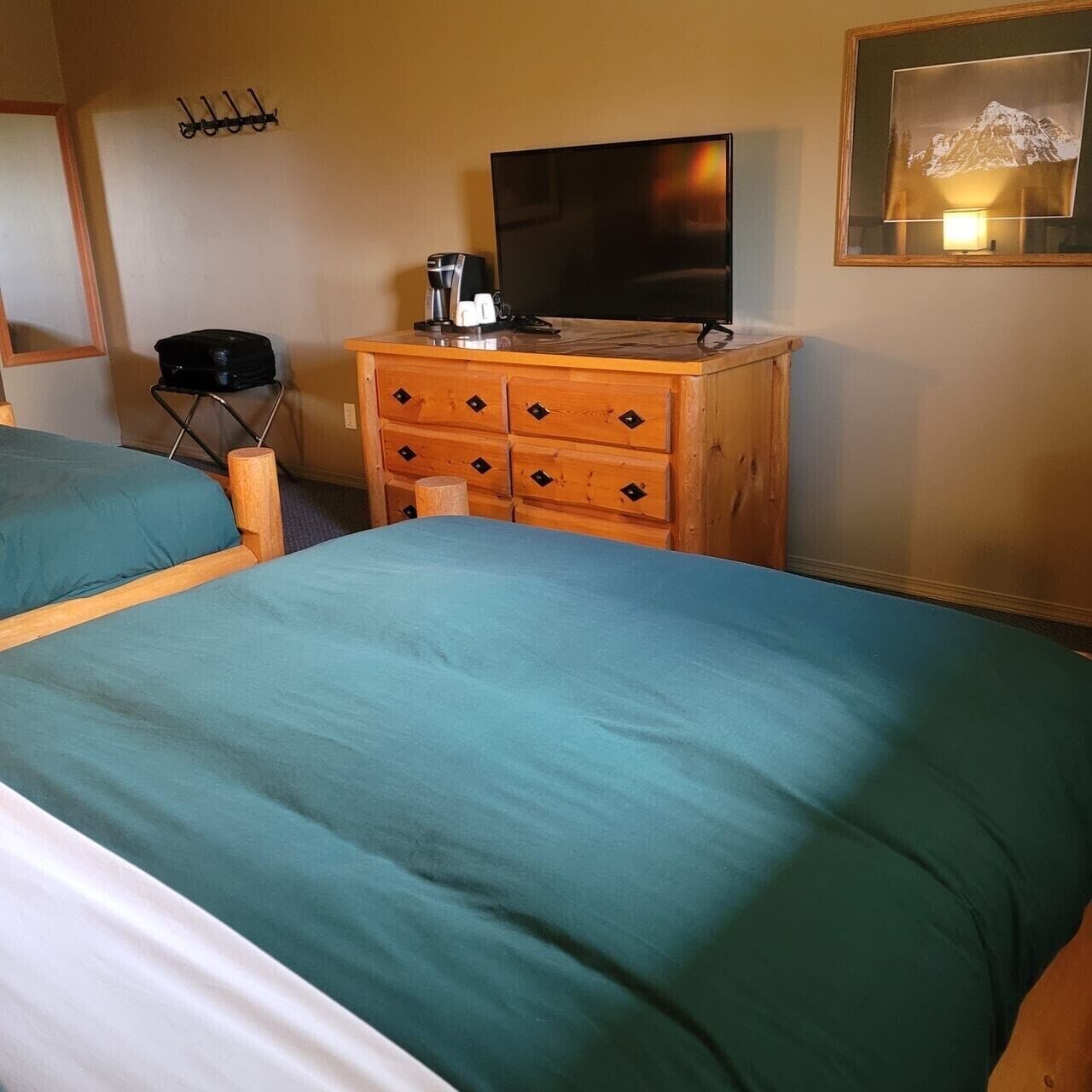 A hotel room with two single beds, a wooden dresser with a flat-screen TV, a coffee maker, and a framed picture on the wall.