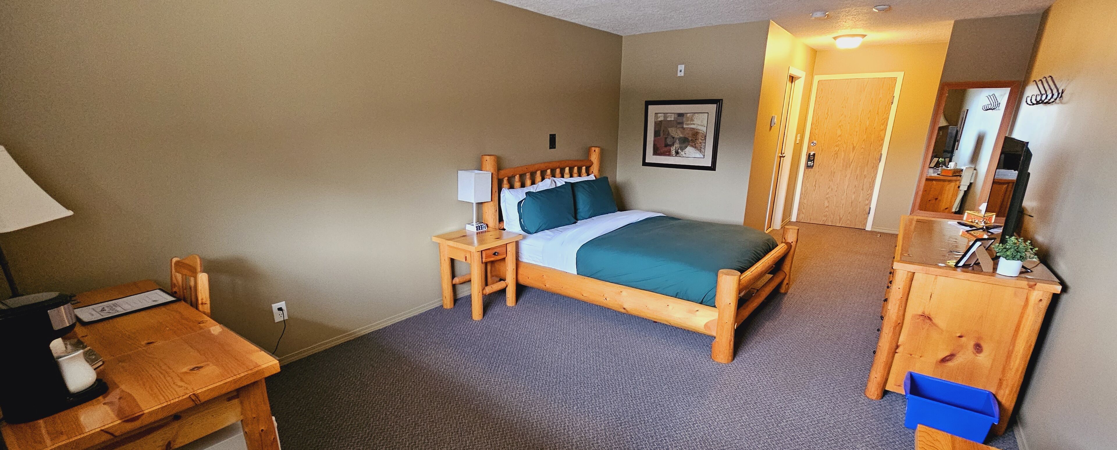A bedroom with a wooden bed, a nightstand, a desk with a chair, a dresser, and a mirror.