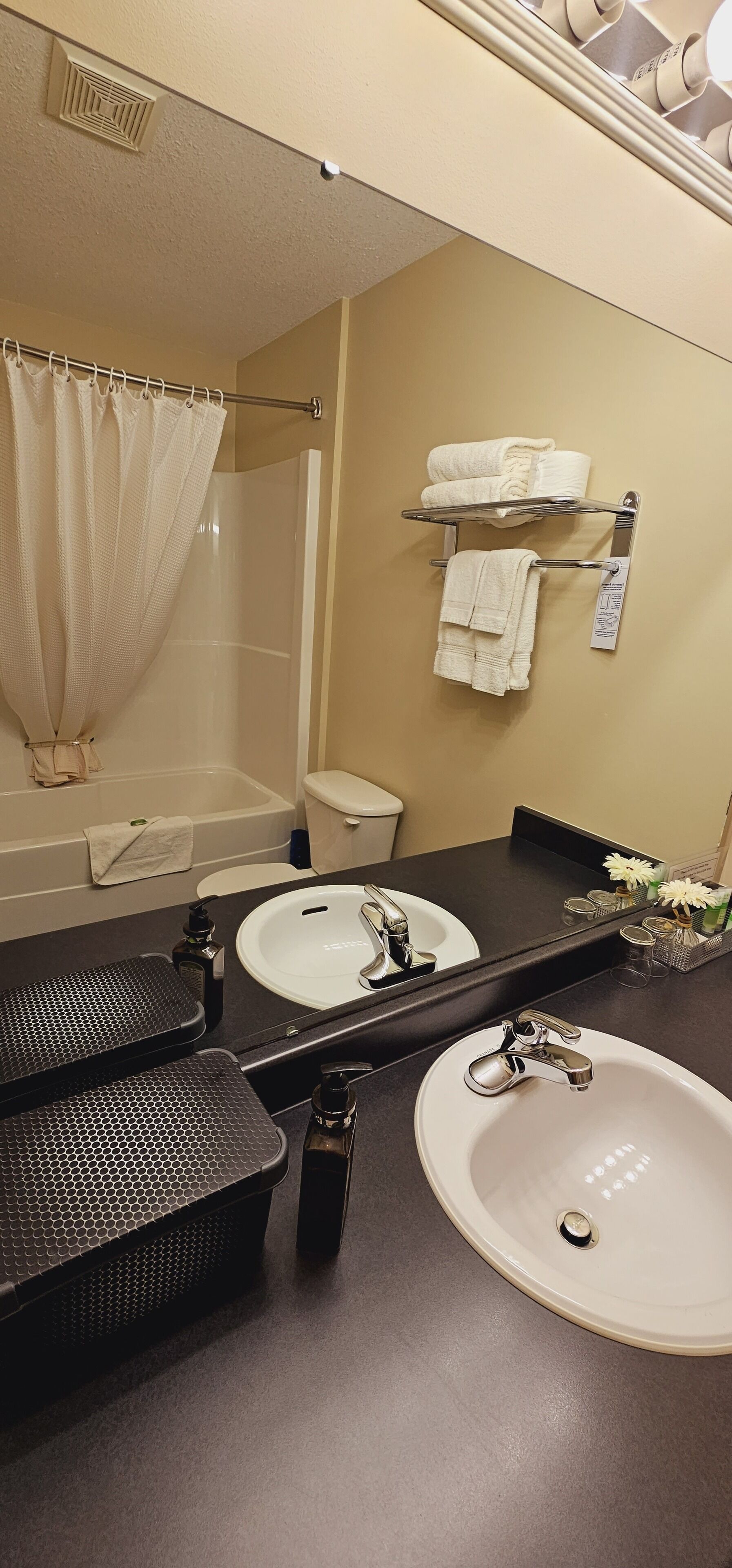 A bathroom with a double sink, a bathtub, a shower curtain, and a towel rack with towels.