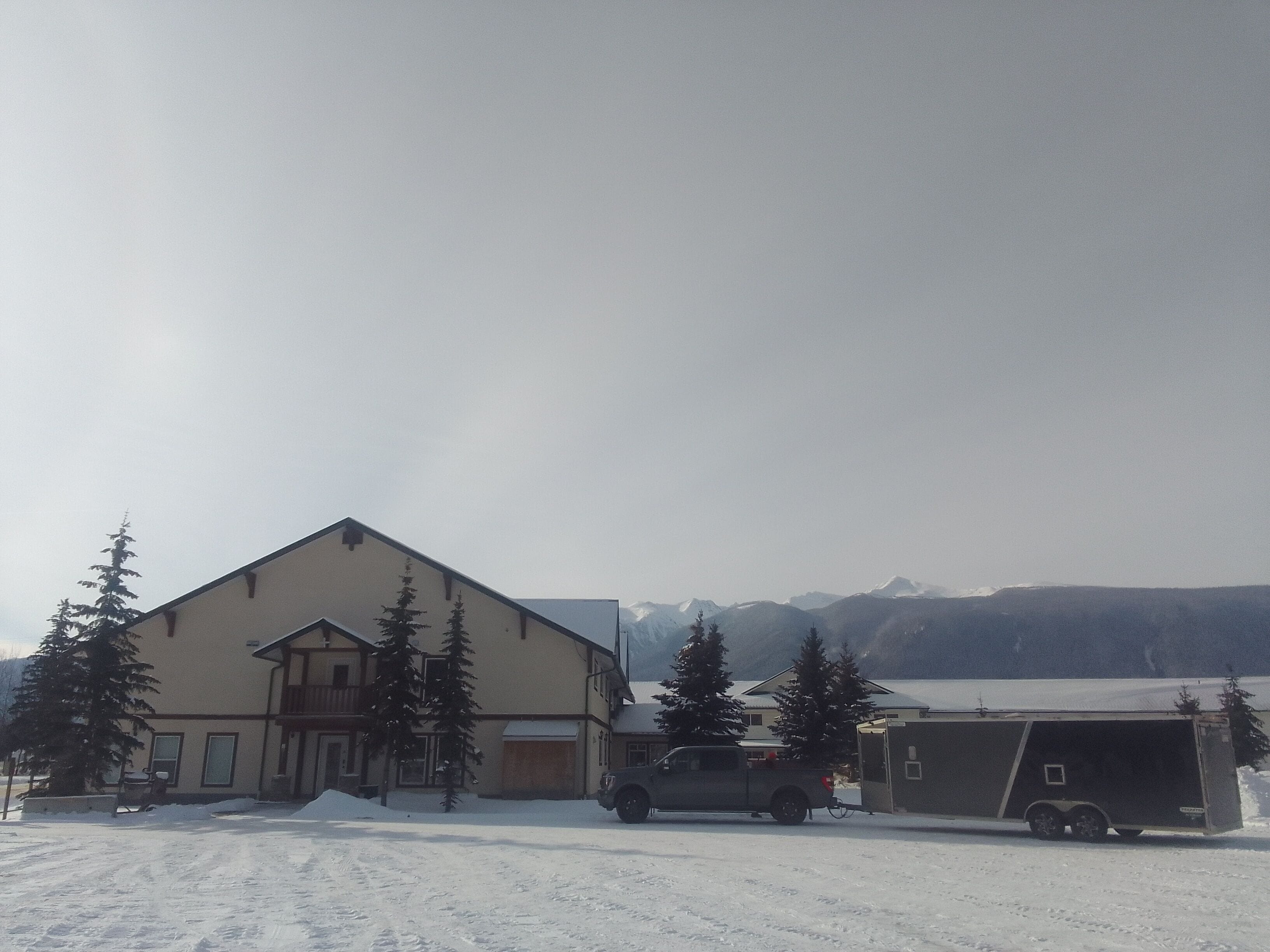 A two-story building with a garage and a trailer in a snowy setting.