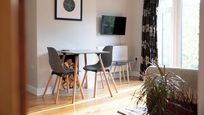 Ein modernes Wohnzimmer mit Essbereich, Kamin, Fernseher und einem großen Fenster mit Vorhängen.