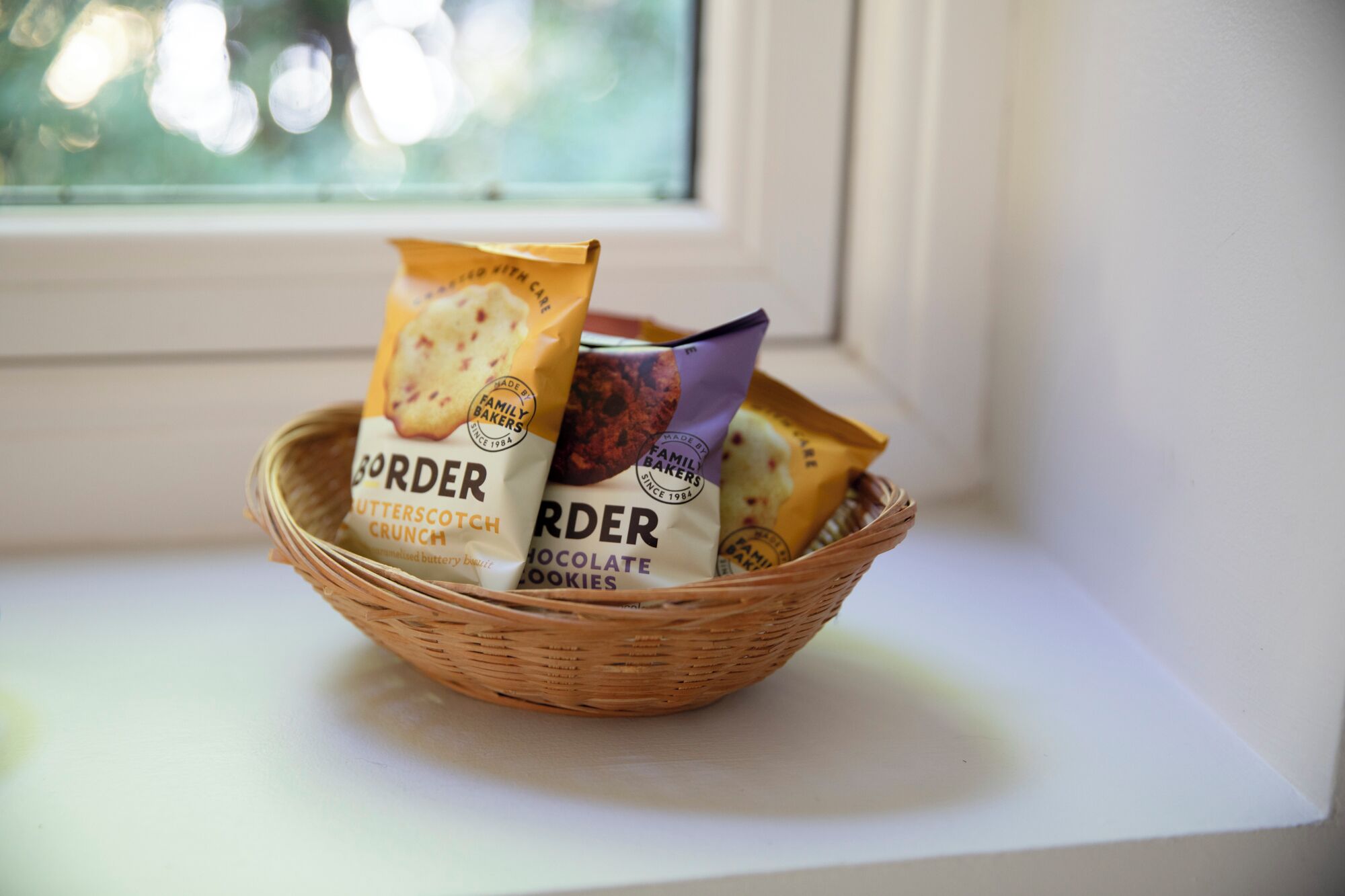 A wicker basket containing three packages of Border snacks on a windowsill.