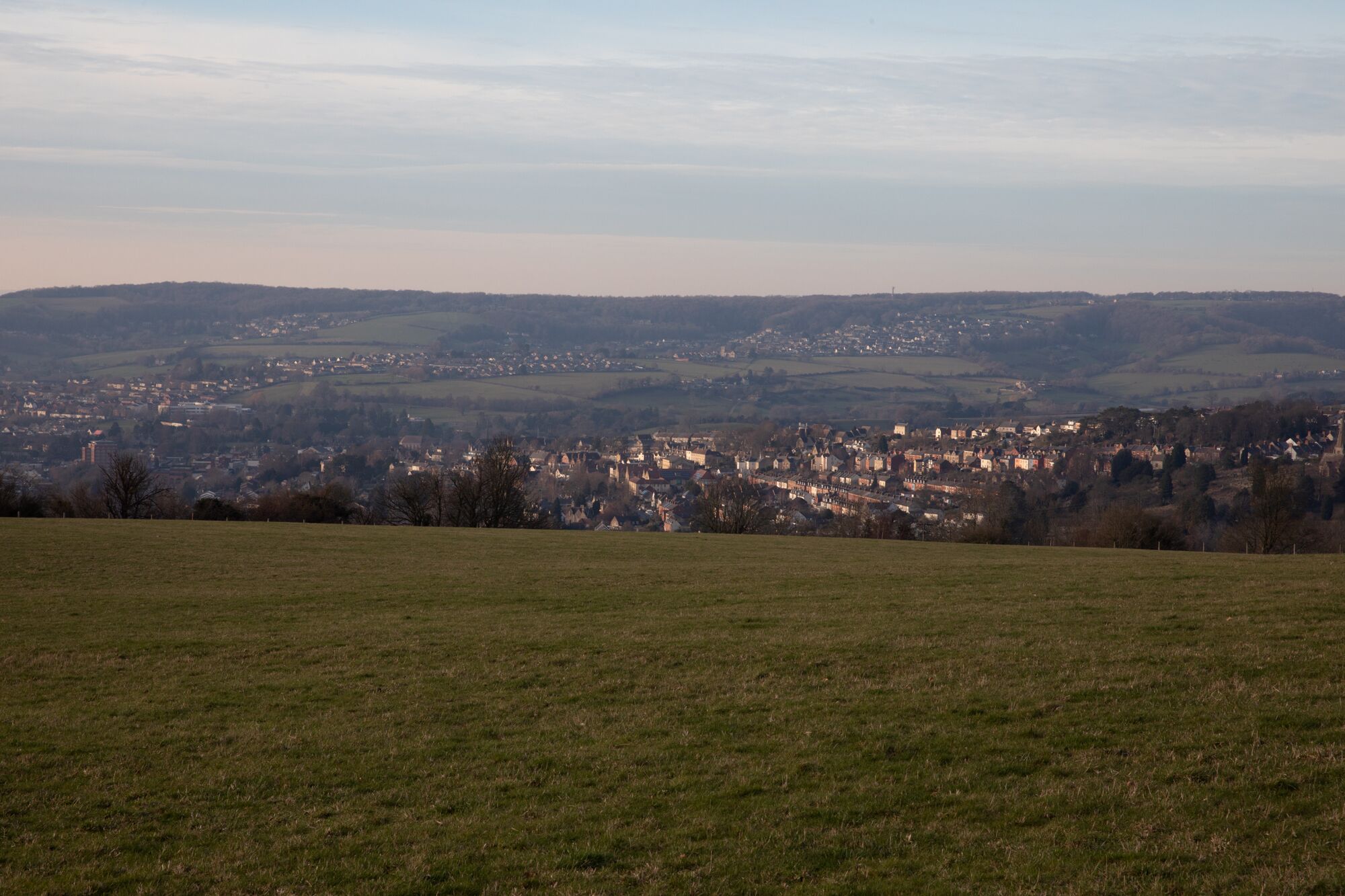 A panoramic view of a town with a large open field in the foreground and a densely built town in the background.