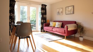 Ein Wohnzimmer mit einem roten Sofa, einem Esstisch mit Stühlen und einem großen Fenster mit Vorhängen.