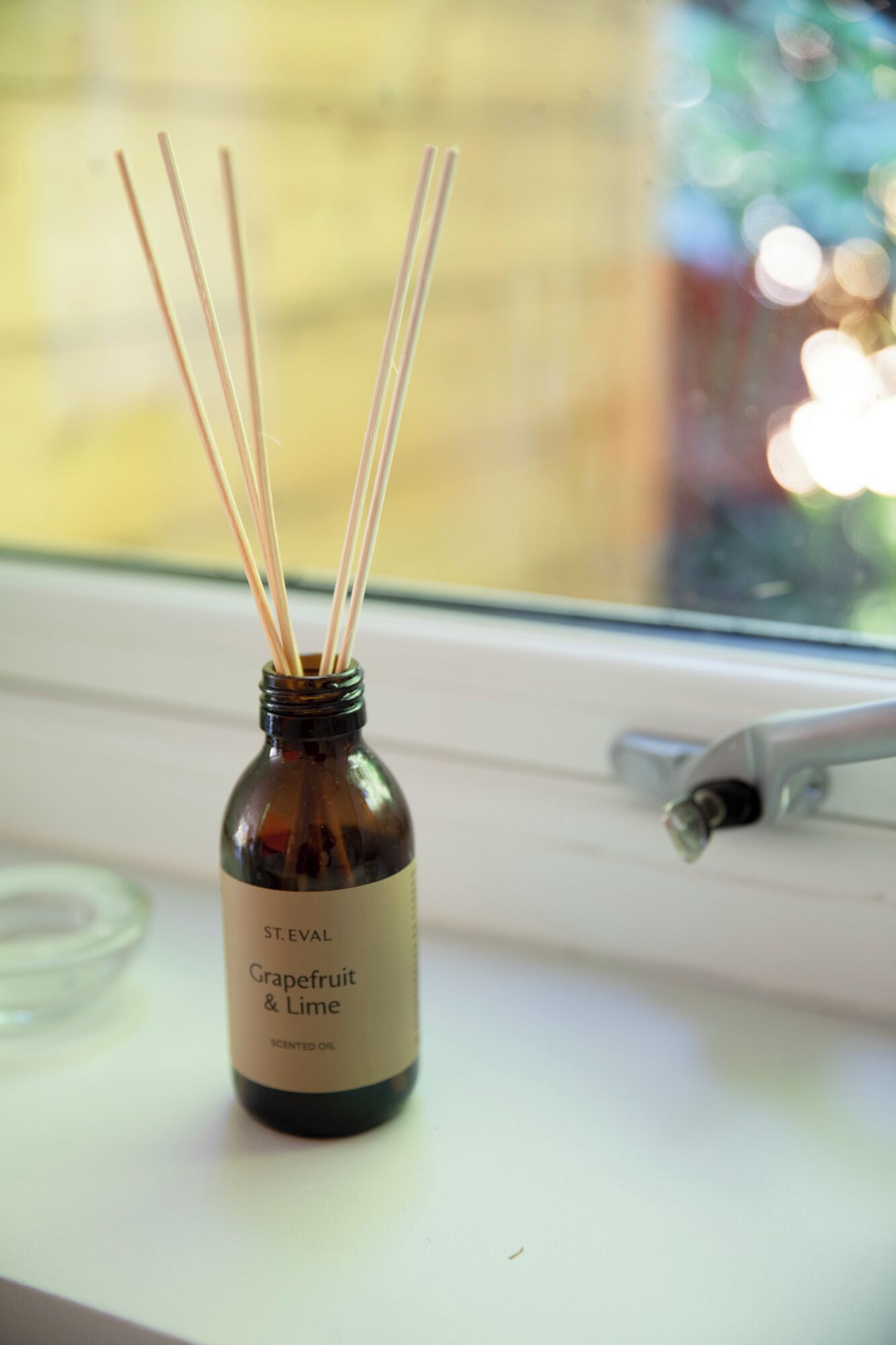 Une bouteille d’huile parfumée à la pamplemousse et au citron vert de la marque St. Eval, posée sur un rebord de fenêtre.