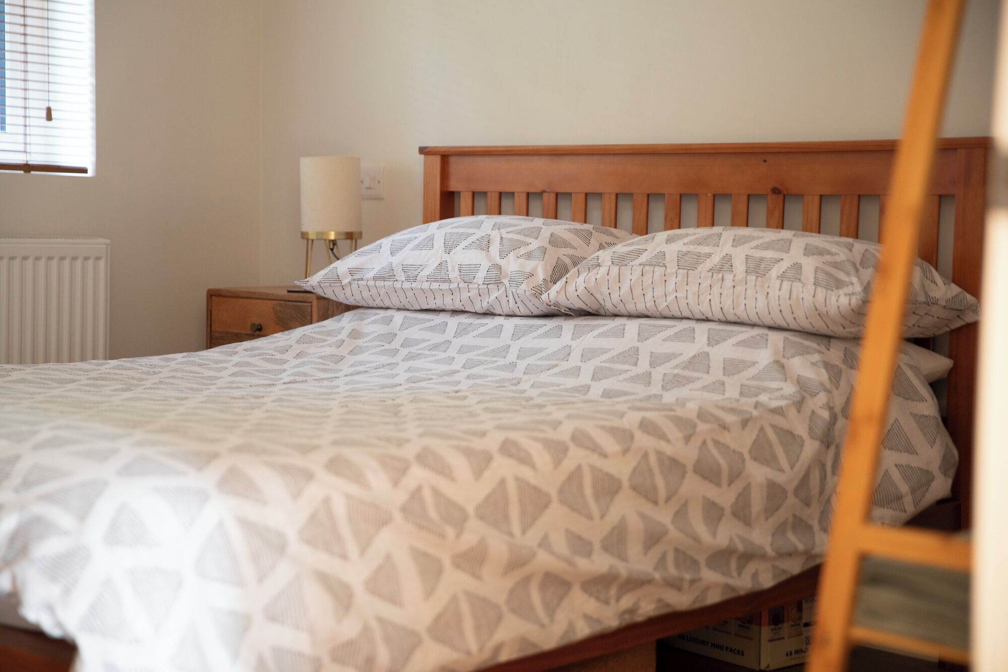 Een net opgemaakt bed met beddengoed met patroon, een houten hoofdbord en een nachtkastje met lamp.