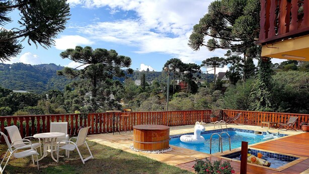 A pool area with a wooden deck, lounge chairs, a bench, and a view of the surrounding landscape. - Suíte Privativa em Jardim1km do Capivari (Campos do Jordão)