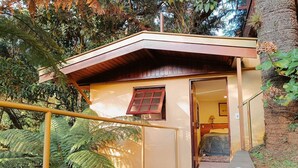 A small building with a wooden door and a window, surrounded by greenery. - Suíte Privativa em Jardim1km do Capivari (Campos do Jordão)