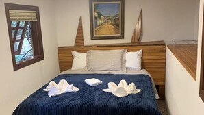 A hotel room with a bed, a painting on the wall, and a window with blinds. - Suíte Privativa em Jardim1km do Capivari (Campos do Jordão)