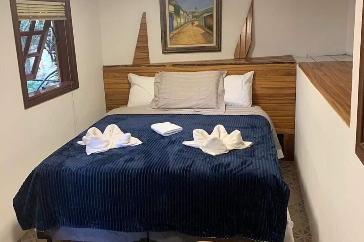 Una habitación de hotel con una cama, un cuadro en la pared y una ventana con persianas.