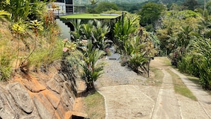 A house with a red roof, surrounded by lush greenery and a stone retaining wall. - Villa Costa Pura Vida (Ciudad Cortés)