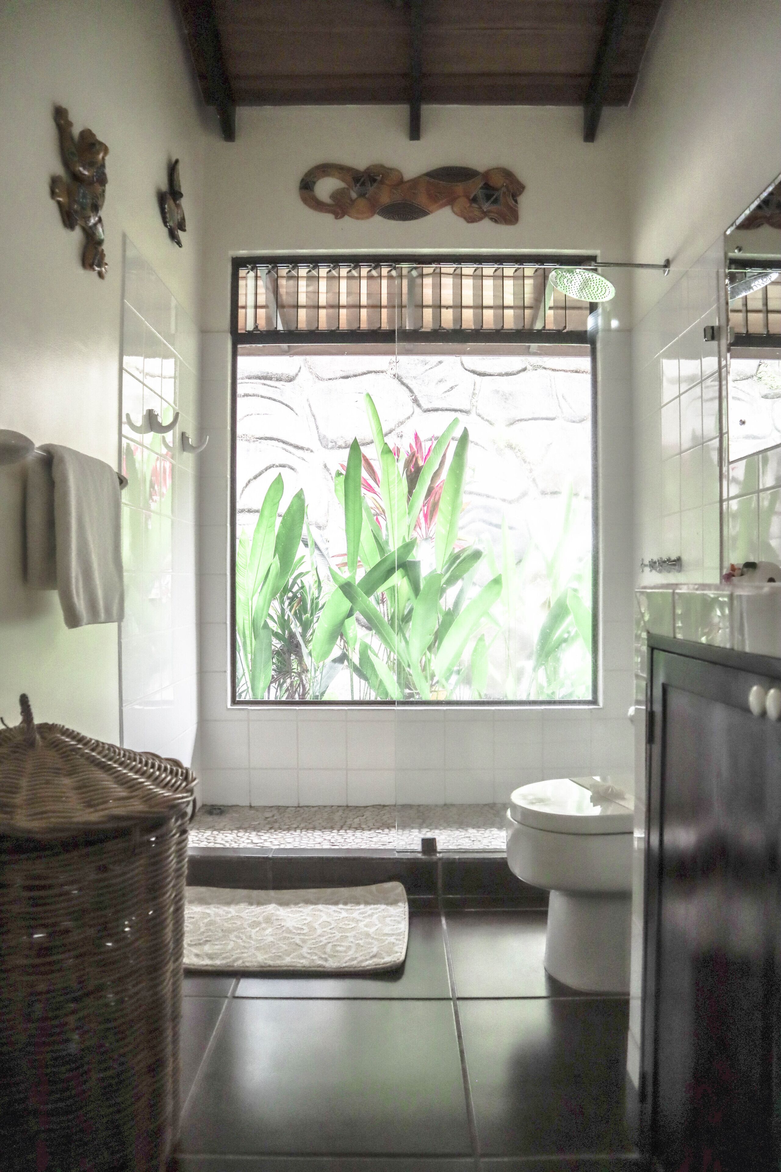 Een badkamer met een groot raam, toilet, wastafel en spiegel.