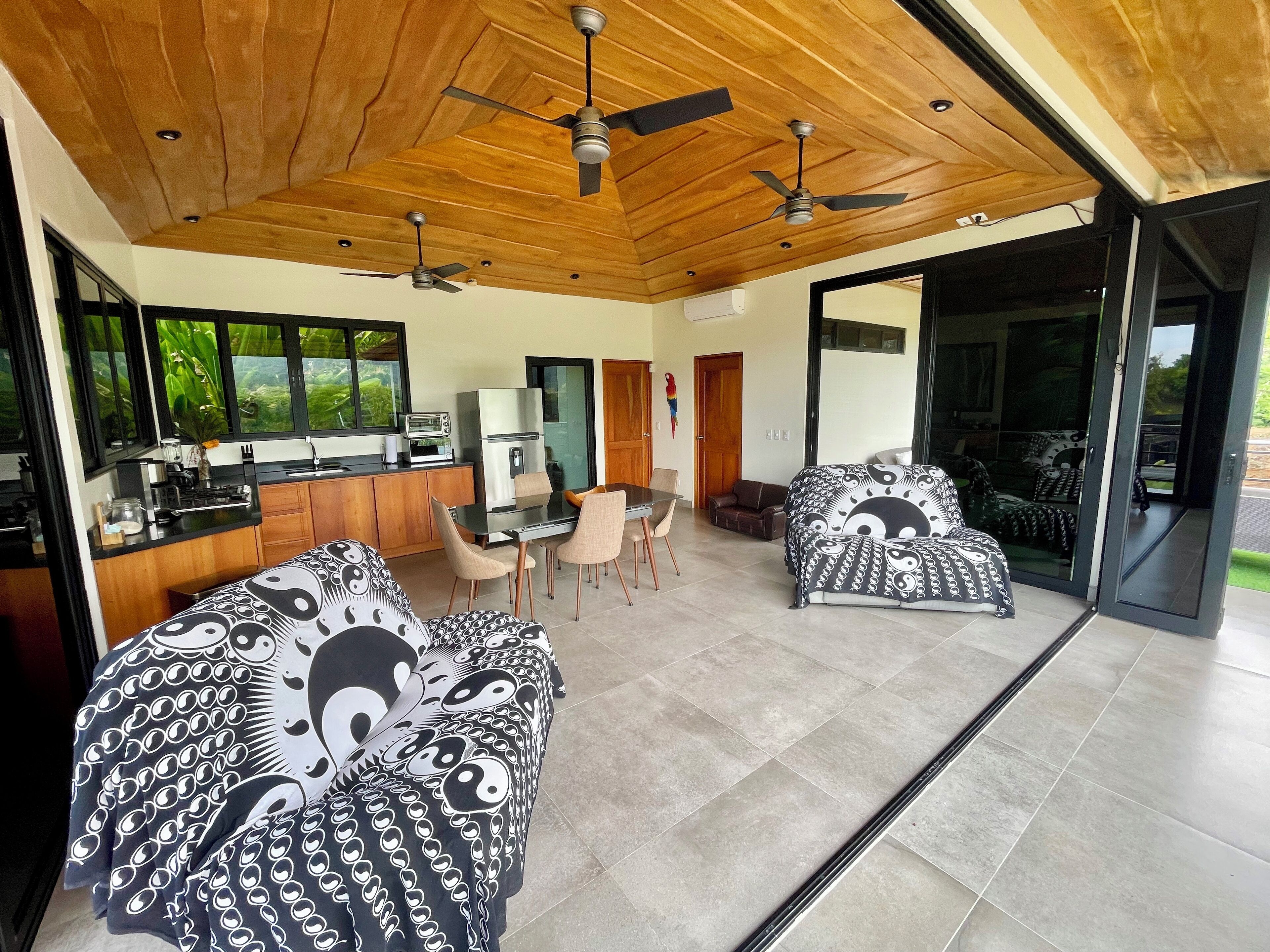 A modern kitchen with a built-in oven, a dining area with a table and chairs, and a living area with patterned sofas.