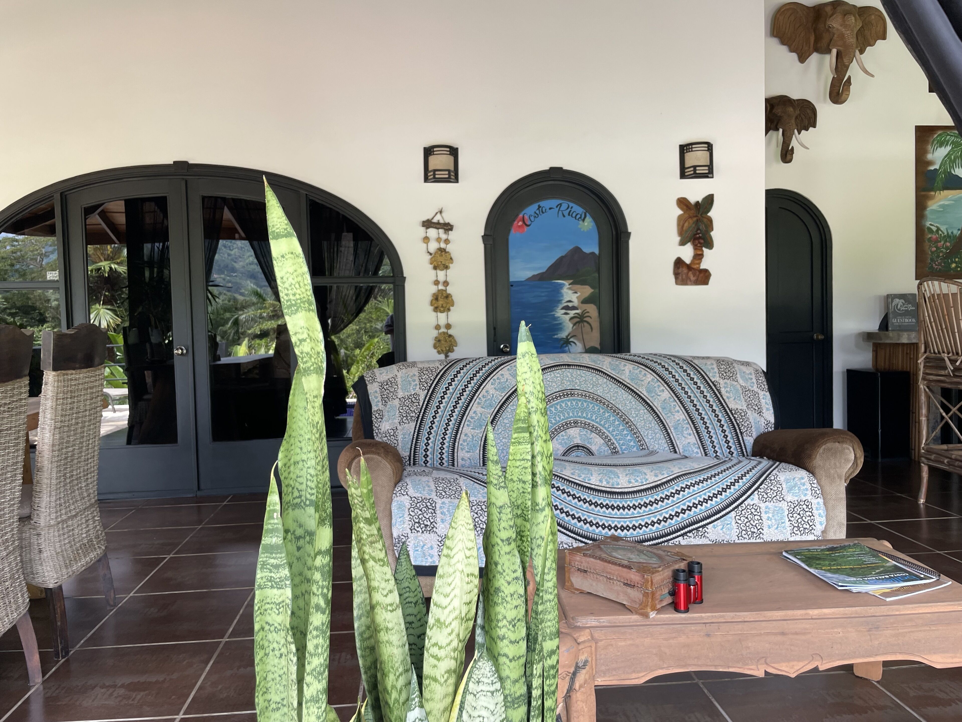 A cozy lounge area with a patterned sofa, a wooden coffee table, and a large window with a view of palm trees.