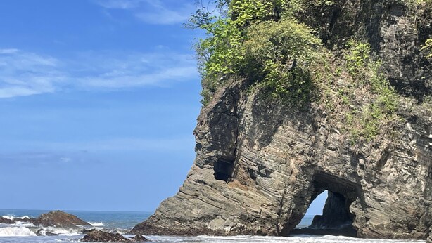 A beach with a rocky cliff featuring a natural archway. - Villa Costa Pura Vida (Ciudad Cortés)
