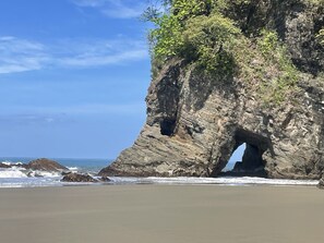 A beach with a rocky cliff featuring a natural archway. - Villa Costa Pura Vida (Ciudad Cortés)