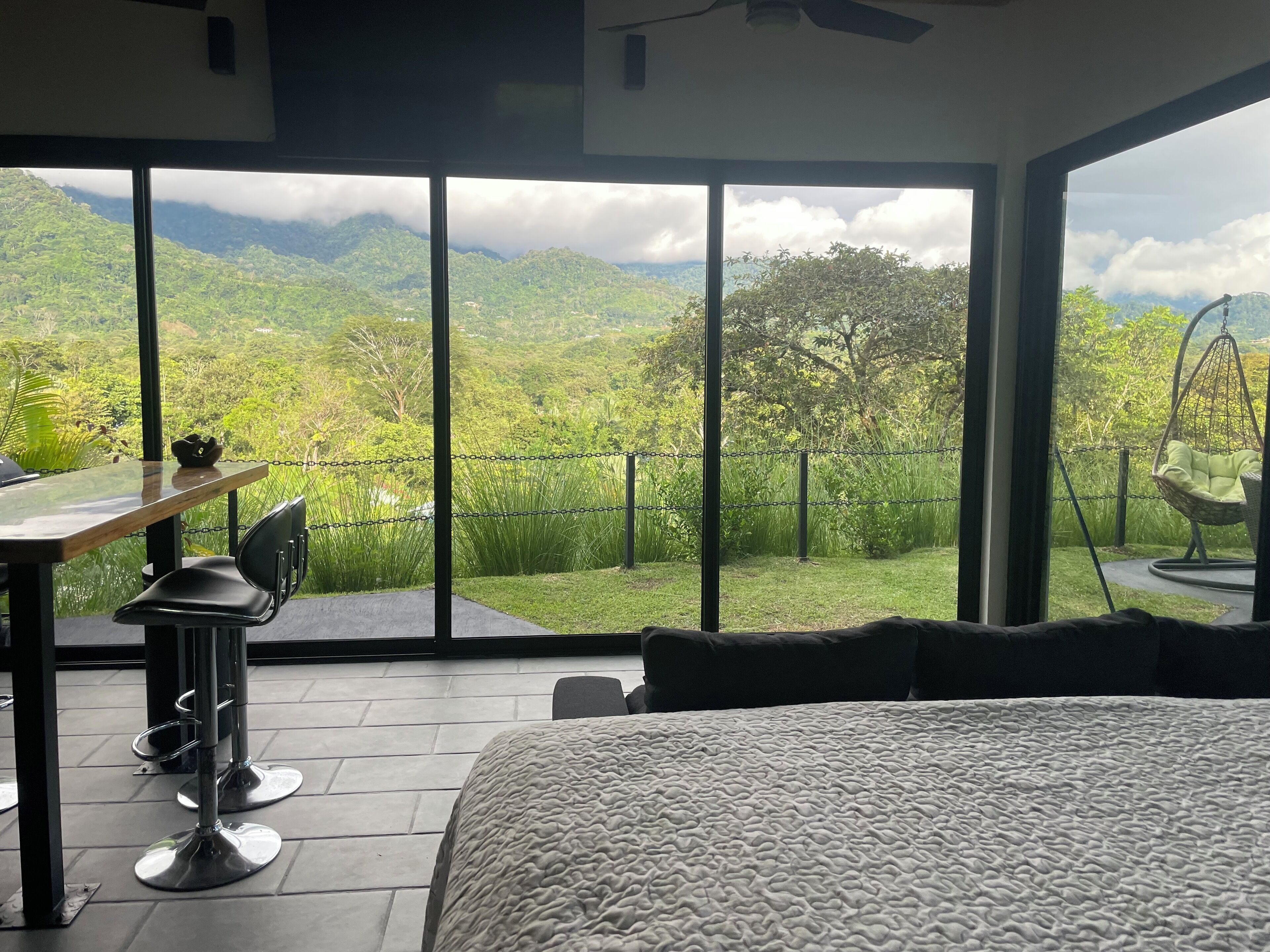 A bedroom with a large window offering a mountain view, a hanging chair, and a dining area with a table and chairs.