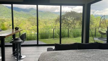 A bedroom with a large window offering a mountain view, a hanging chair, and a dining area with a table and chairs.