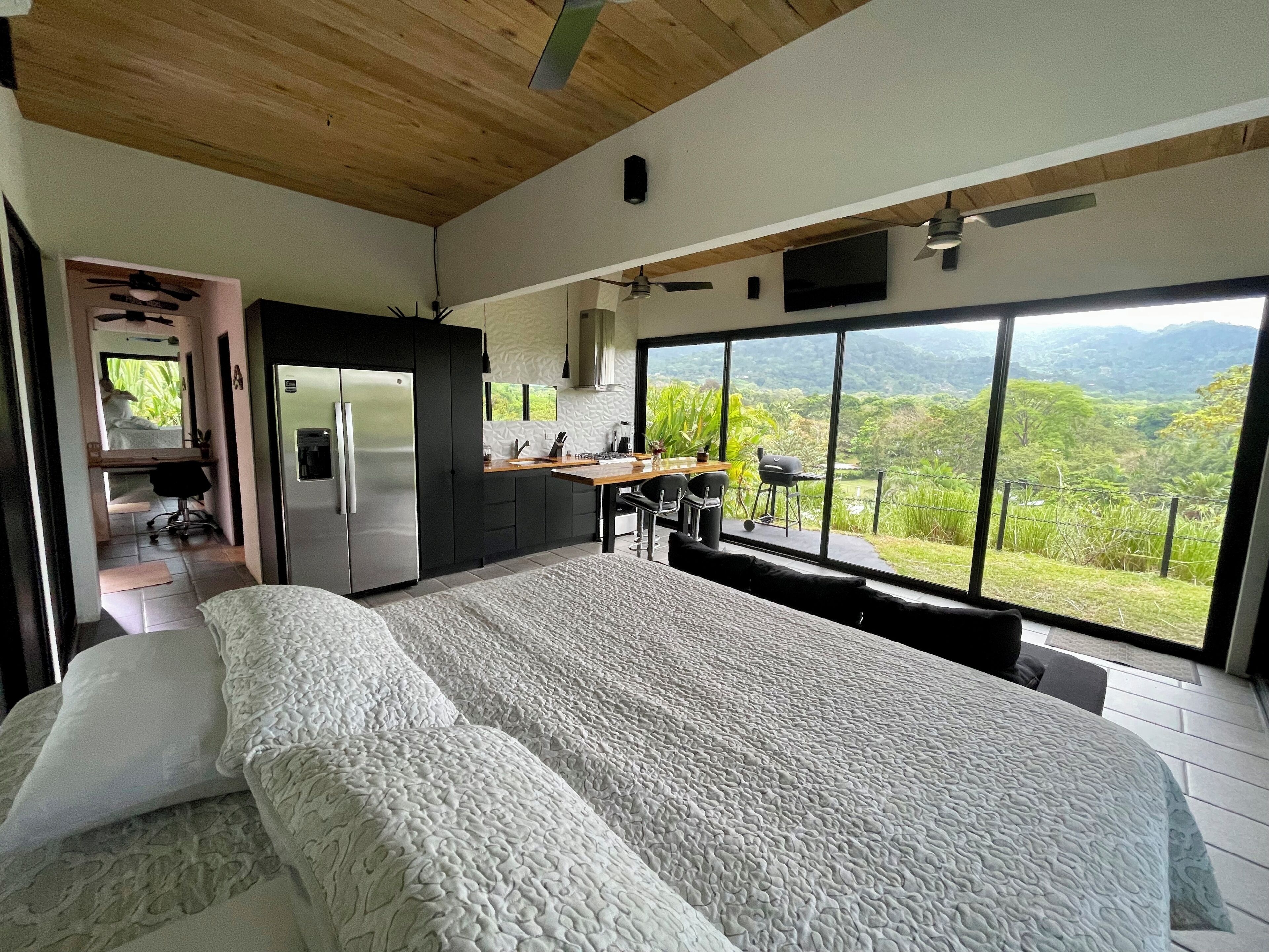 Un dormitorio con una cama grande, una kitchenette y vistas a un paisaje exuberante.