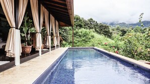 A rectangular pool with a tiled edge, surrounded by a covered area with curtains and potted plants. - Villa Costa Pura Vida (Ciudad Cortés)