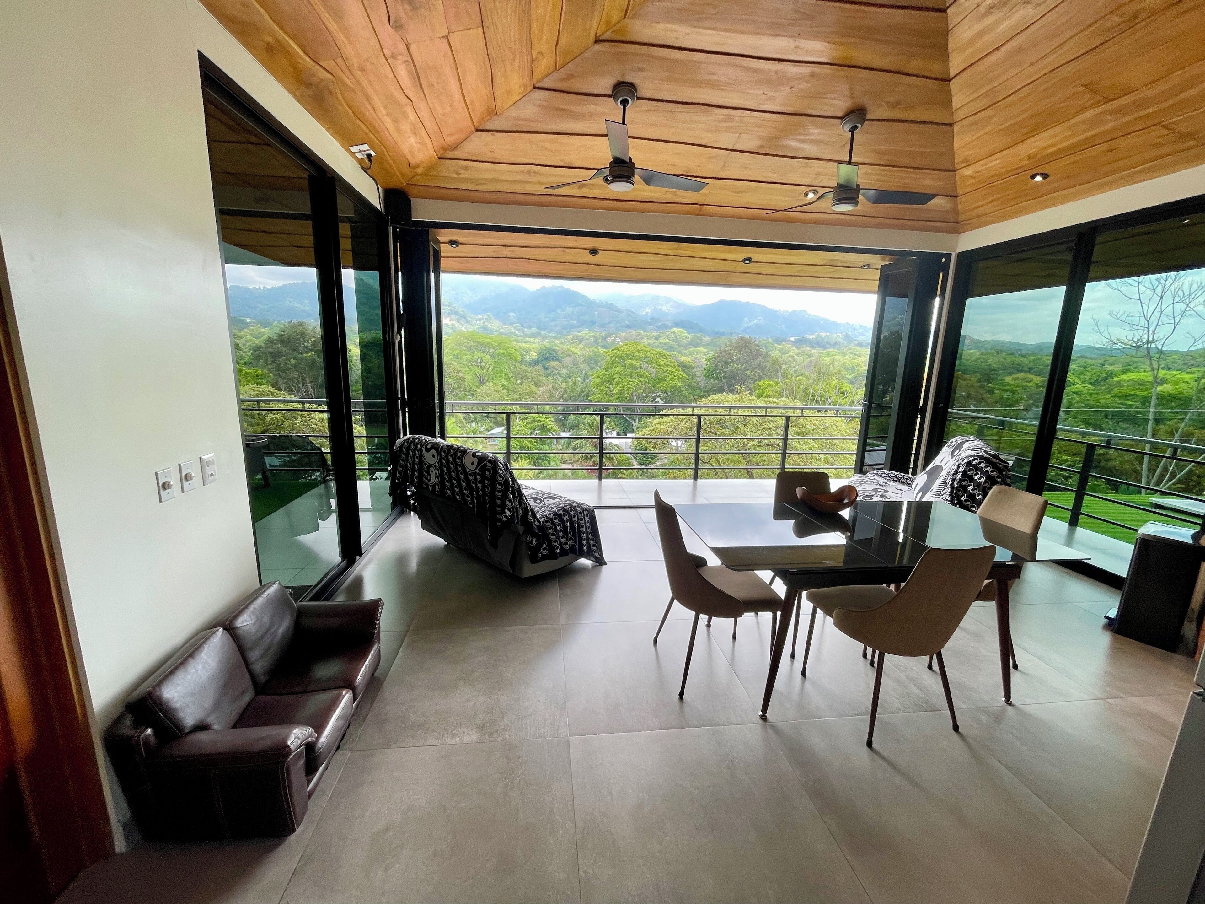 Un interior moderno con zona de comedor, un sofá y vistas a un paisaje exuberante.