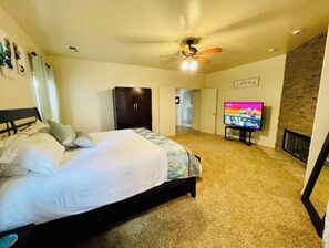 Une chambre à coucher comprenant un lit, un t éléviseur, un ventilateur de plafond et une cheminée.