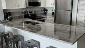 Una cocina moderna con armarios blancos, electrodomésticos de acero inoxidable, una encimera de granito y cuatro taburetes de bar.