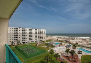 A high-rise hotel with a tennis court, swimming pool, and beach view.