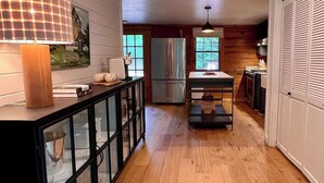 Une cuisine avec un plancher en bois, un réfrigérateur, une table à manger et un meuble avec des portes en verre.