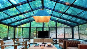 Une véranda avec un toit en verre, une télévision, des meubles en bois et des livres.