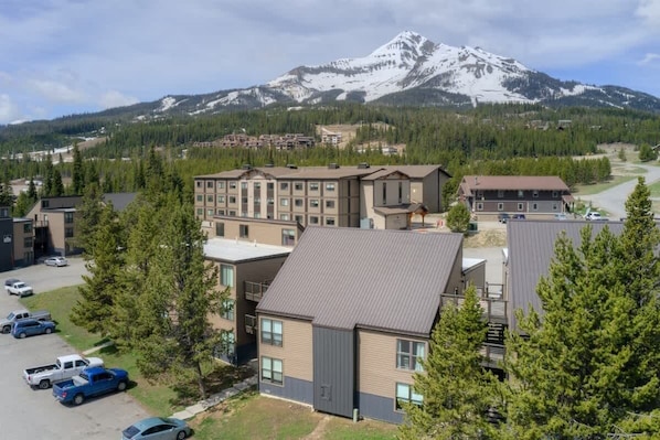 A hotel with multiple buildings, a parking lot, and a mountain in the background. - 2 Bedroom With Loft Located in Big Sky Resort Area (Big Sky)