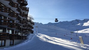 Un centro de esquí con un teleférico, pistas cubiertas de nieve y un edificio con balcones.