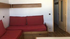 Una habitación pequeña con un sofá rojo, un estante de madera y una puerta que da a otra habitación.