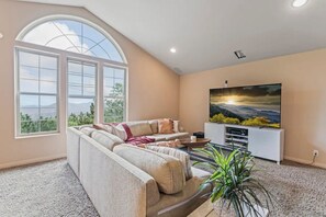 Relax in this spacious living room with a high ceiling, large windows, and a comfortable sectional sofa.