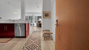 Eine moderne Küche mit Geschirrspüler, einer Holztür und einem gemusterten Teppich, der zum Essbereich führt.