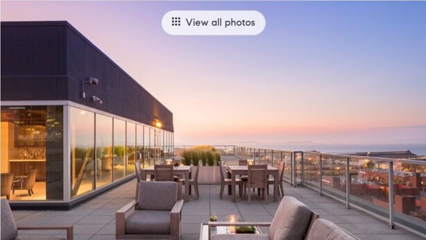 Eine Dachterrasse mit Sitzgelegenheiten im Freien, einem Feuerkorb und Blick auf die Skyline im Abendlicht.
