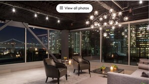 Ein moderner Lounge-Bereich mit Ledersesseln, einer Couch und einem Couchtisch, mit großen Fenstern und Blick auf die Stadt.