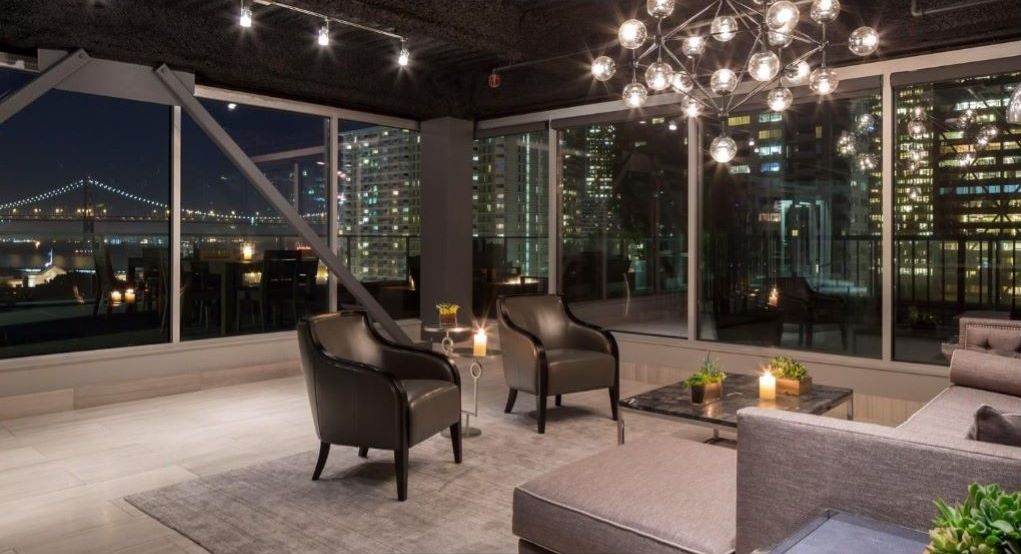 A modern lounge area with leather chairs, a sofa, and a coffee table, featuring large windows with a cityscape view.
