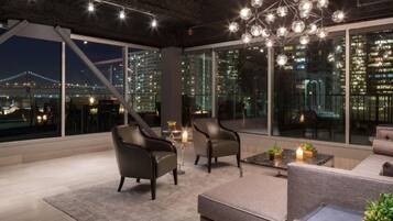 A modern lounge area with leather chairs, a sofa, and a coffee table, featuring large windows with a cityscape view.