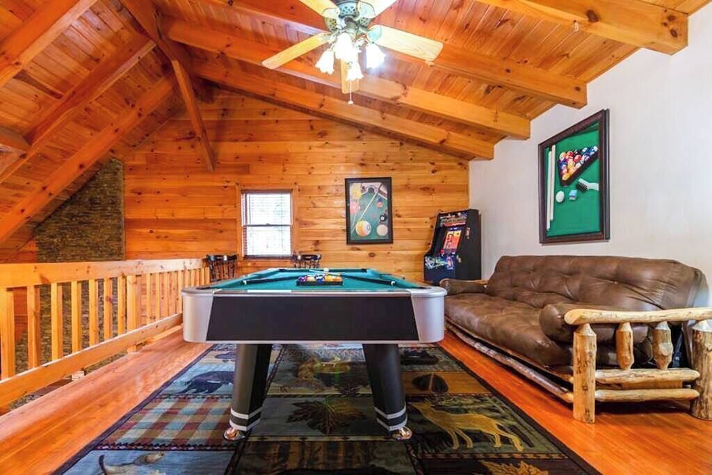 A cozy room with a pool table, a brown leather sofa, and a ceiling fan.