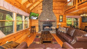 A cozy cabin interior with a stone fireplace, wooden walls, leather seating, and large windows. - Pigeon Forge Cabin /Game Room/Dog Friendly/Hot Tub (Pigeon Forge)