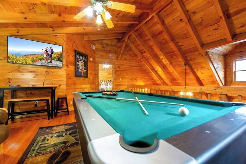 A pool table in a wooden room with a ceiling fan, a television, and a bench.
