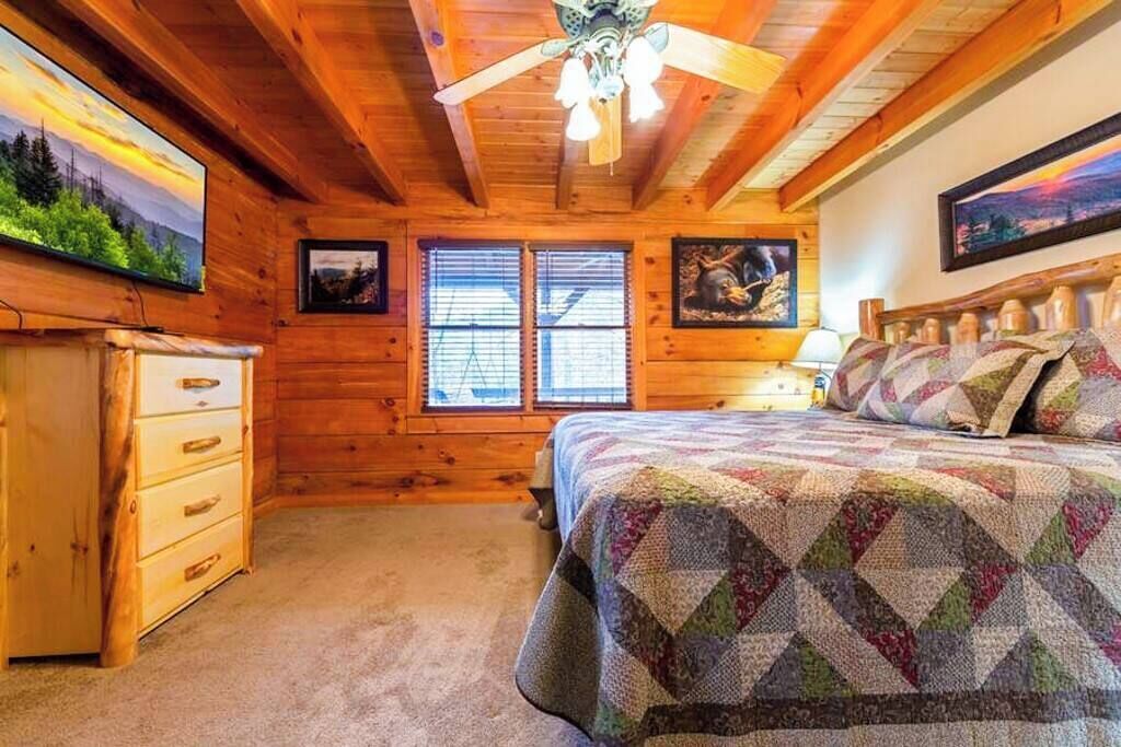 Un dormitorio rústico de cabaña de madera con cama, cómoda y ventilador de techo.
