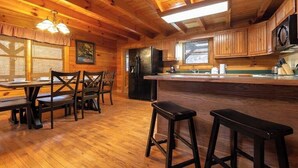 A wooden cabin interior with a kitchen area, dining table, and bar stools. - Pigeon Forge Cabin /Game Room/Dog Friendly/Hot Tub (Pigeon Forge)