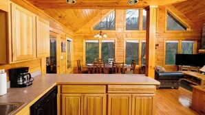 A wooden cabin interior with a kitchen, dining area, and a fireplace.