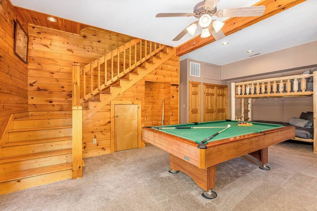 Un interior de madera con mesa de billar, escalera y ventilador de techo.