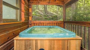 A wooden cabin with a hot tub and a large window overlooking a forest.