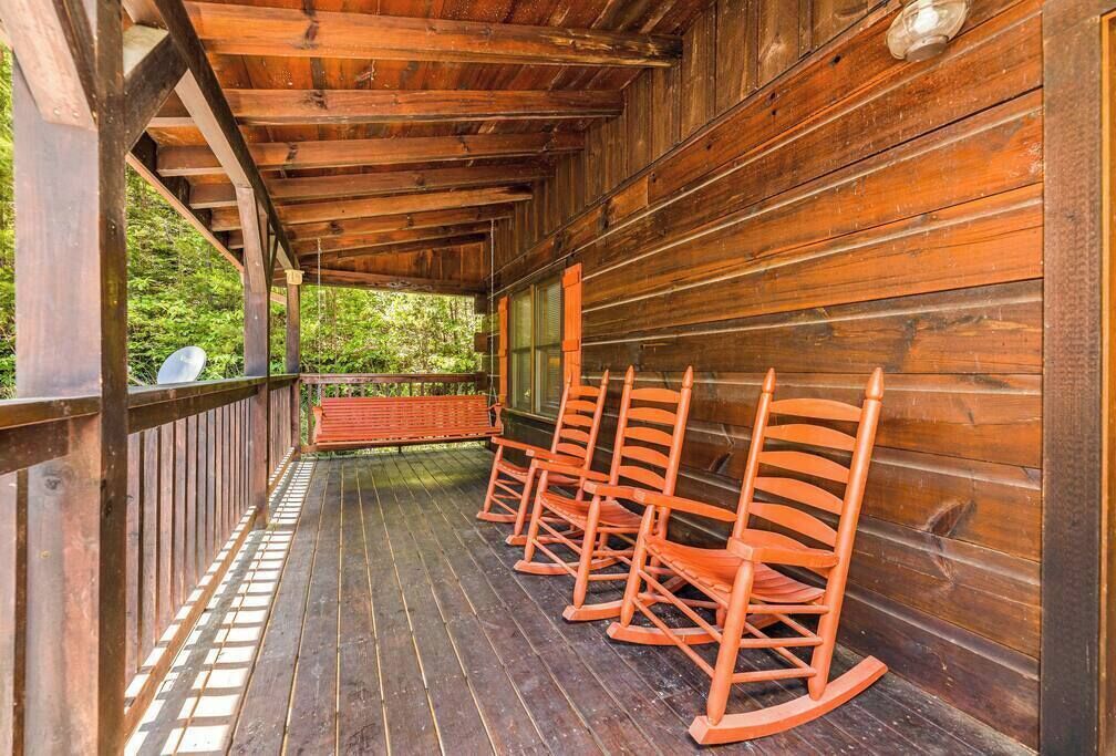 Een houten veranda met schommelstoelen en een bank, met uitzicht op een weelderig groen landschap.