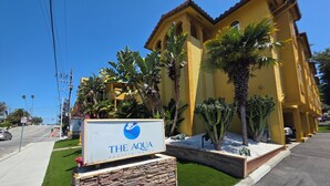 A hotel sign with a logo and name, surrounded by a well-maintained garden with various plants and a stone wall. - The Aqua Pacific Hotel (Santa Cruz)